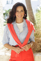 An older brunette woman wearing a blue-and-white striped shirt with a salmon-coloured jumper and trousers