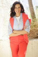 An older brunette woman wearing a blue-and-white striped shirt with a salmon-coloured jumper and trousers