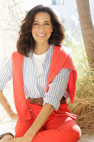 An older brunette woman wearing a blue-and-white striped shirt with a salmon-coloured jumper and trousers