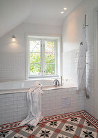 Badewanne im Badezimmer mit weißen Wandfliesen und gemusterten Bodenfliesen
