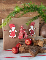 Verpacktes Geschenk mit DIY-Papiernikolaus, Holzsterne und Äpfel im Vordergrund