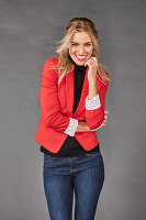 A blonde woman wearing a black turtleneck, a red blazer and jeans