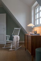 A rocking chair and a chest of drawers in front of an attic window