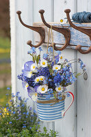 Spring bouquet of forget-me-nots, grape hyacinths, daisies, and horned violets hung in a cup on a coat hook
