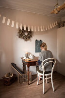 Frau sitzt am alten Holztisch, darüber DIY-Wimpelkette und Kranz an der Wand