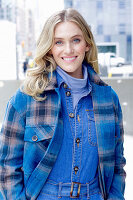 Junge blonde Frau in blauem Jeansoverall und karierter Jacke