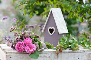 Liegender Strauß aus Rosen, Sterndolde und Oreganoblüten, Zweig mit Stachelbeeren und Vogelhaus