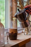 Frauenhand giesst Kaffee aus Espressokanne in Becher