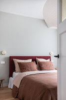 Bett in sanften Rottönen im schlichten Schlafzimmer