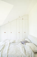 Custom, fitted wardrobes and double bed in white bedroom with sloping ceiling
