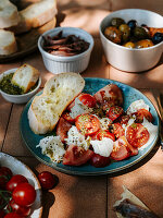 Ready dish of mozzarella and tomatoes, with bread, olives and anchovies