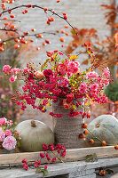 Rosarot-pinker Herbststrauß aus Rosen, Hagebutten und Zweigen vom Pfaffenhütchen, graue Speisekürbisse