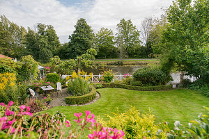 Well tended garden with flowers, box hedges, and a lawn, with a river in the background