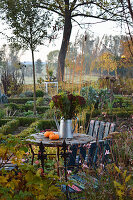 Gießkanne mit Herbstblumen und Kürbissen auf Tisch im Garten