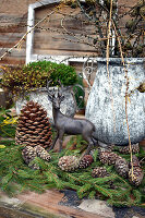 Hirschfigur, Nadelzweige und Zapfen vor alten Töpfen auf Gartentisch
