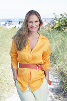 Langhaarige Frau in orangefarbener Bluse mit Gürtel am Strand