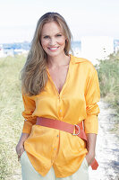 Long haired woman in orange blouse with belt sitting on the beach