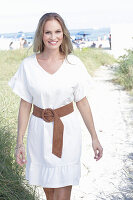 Langhaarige Frau in weißem Sommerkleid mit Gürtel am Strand