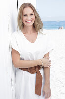 Langhaarige Frau in weißem Sommerkleid mit Gürtel am Strand