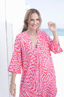 Langhaarige Frau in pink gemustertem Kleid am Strand