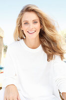 A young woman on a beach wearing a long-sleeved white top and shorts