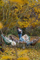 Seat under maple tree in autumnal garden, and a woman with dog in the background