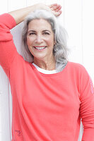 A mature woman with grey hair wearing a salmon-pink jumper