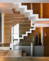 White staircase with modern glass balustrade in front of wood-panelled wall in apartment