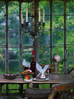 Old wooden table with cake and berry juice, above candlestick chandelier in the greenhouse