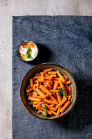 Bowl of whole baked baby carrot with yogurt sauce on blue tablecloth over grey background