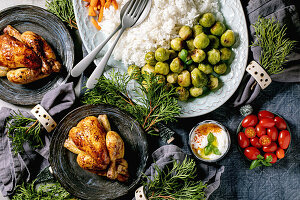 Christmas dinner table with grilled mini chicken, rice and vegetables baked brussel sprouts, baby carrot in ceramic bowls