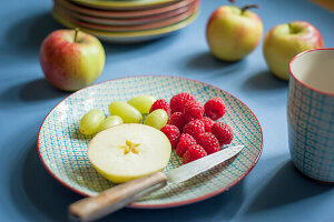 Apple, grapes and raspberries with a knife on a ceramic plate