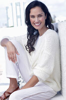 Dark haired woman in white top, white wrap cardigan and white trousers