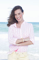 Brünette Frau in rosa gestreifter Bluse und heller Hose am Strand