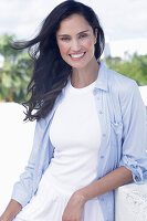 Dark-haired woman in a white top, light blue shirt and white trousers