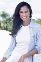 Dark-haired woman in a white top, light blue shirt and white trousers