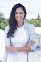 Dark-haired woman in a white top, light blue shirt and white trousers