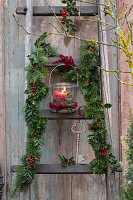 Weihnachtlich dekorierte Holzleiter mit Girlande aus Ilex 'Blue Princess', Tannenzweigen (Abies), Windlicht und Schlüssel