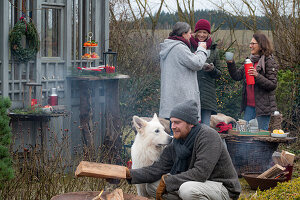 Man and dog around fire pit, in the background women with mulled wine