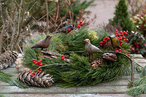 Wreath with pine branches (Pinus), holly berries (Ilex verticillata) and wooden birds