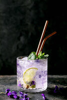 Glass of lemonade soda cocktail with violets flower ice and lime