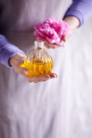 Woman holding a perfume bottle with aromatic oil and a peony blossom