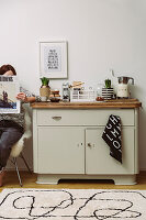 Vintage chest of drawers with kitchen items, person sitting on chair and reading