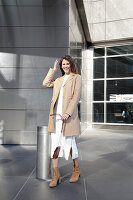 A brunette woman wearing a white knitted dress and beige leather coat