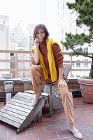 A brunette woman wearing an autumn outfit with a yellow knitted jumper over her shoulders