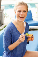 Blonde Frau in blauem Shirt mit Dessert in der Hand