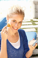 Blonde woman in blue shirt applying makeup with brush