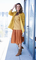 Long haired woman in orange skirt, yellow knit sweater and short coat
