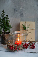 Lantern with a wreath of holly berries, behind it mini conifers and presents