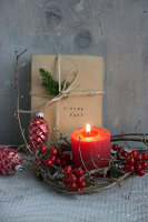 Candle in a wreath of holly berries with wrapped Christmas gift